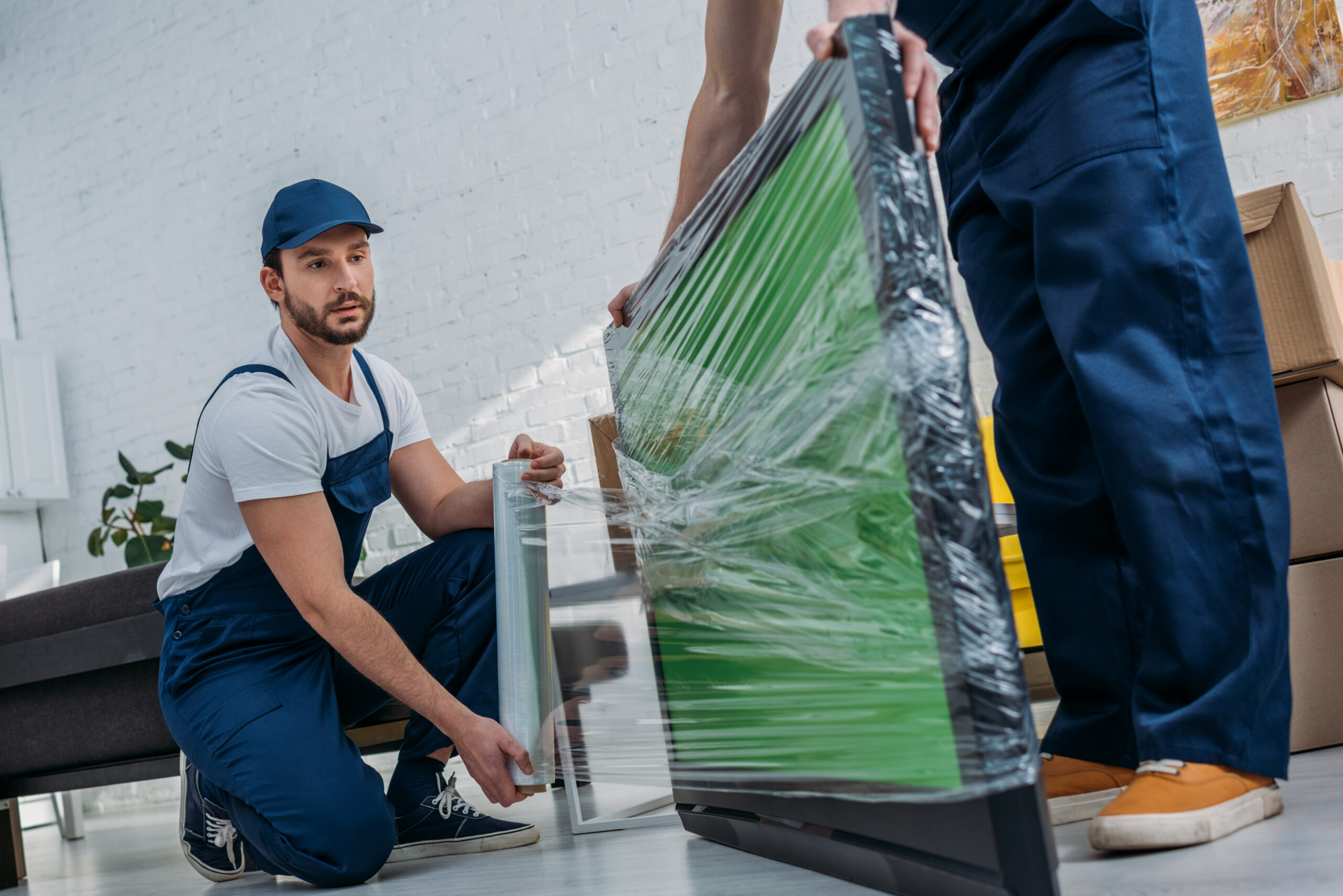 two movers using roll of stretch film while wrapping tv with green screen in apartment installation d'écran d'affichage